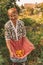 Cheerful senior woman picking organic ripe yellow tomatoes in apron of traditional rural clothes