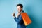 Cheerful shopper holding orange shopping bag on shoulder, turn around at camera with thumbs up, recommending store, blue