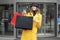 Cheerful shopper woman holding shopping bags at the exit from the mall. Her finger shows on the mockup black bag.