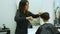 Cheerful skillful barber making a haircut with scissors to a young bearded man