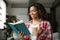 Cheerful smart pretty black young woman student reading book, enjoy cup of hot favorite drink, study