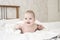 Cheerful smiling baby on white towel after bathing. The child laughs lying on his stomach. Girl boy half a year. Portrait of