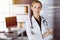 Cheerful smiling female doctor standing with arms crossed in clinic. Portrait of friendly physician woman. Medicine