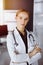 Cheerful smiling female doctor standing with arms crossed in clinic. Portrait of friendly physician woman. Medicine