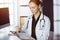 Cheerful smiling female doctor using clipboard in clinic. Portrait of friendly physician woman at work place. Medicine