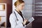 Cheerful smiling female doctor using tablet computer in sunny clinic. Portrait of friendly physician woman at work