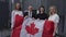 Cheerful smiling man and women looking at camera holding Canadian flag standing outdoors. Group of young business team