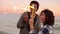 Cheerful smiling multiethnic couple holding burning sparkling candles standing by the sea during sunset