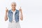 Cheerful, smiling old caucasian woman in denim vest over dress, grinning happy pointing fingers up, recommend product