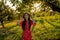 Cheerful smiling red head teen girl with freckles in red dress standing among the garden and looking at the camera