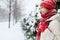 Cheerful smiling woman in white down jacket and red cap, scarf and mittens sitting on a bench in the alley on the snowy street