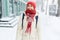 Cheerful smiling woman in white down jacket and red cap, scarf and mittens walking on the snowy street after blizzard in city