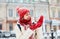 Cheerful smiling woman in white down jacket and red cap, scarf and mittens walking on the snowy street after blizzard in city