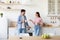 Cheerful smiling young wife and husband with cups of hot drink talk on kitchen interior in morning