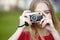 Cheerful smiling young woman holding old retro film camera and taking pictures, copy space, amateur photographer, sunny summer