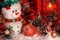 Cheerful snowman and Christmas balls are covered with snow in the light of a red lantern on the background of New Year`s scenery