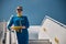 Cheerful stewardess standing on airplane steps under blue sky