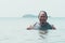 A cheerful and stout asian guy in a tank top holding a bottle of beer while relaxing in chest deep waters at the beach