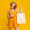 Cheerful Summer Girl Holding White Tote Bag And Pointing At It