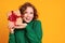 Cheerful surprised   woman  laughs with her mouth open holds a Christmas gifts on a colored yellow background