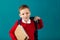 Cheerful thoughtful little school boy in school uniform with backpack and big pile of books standing against blue wall. Looking