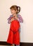 The cheerful three-year-old girl tries on on herself a beautifulred dress on a hanger