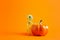 Cheerful toy skeleton with big pumpkin on orange background with copy space