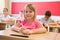 Cheerful tween girl listening to schoolteacher and writing in notebook