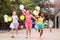 Cheerful tweenagers with balloons in hands running on city street