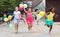 Cheerful tweenagers with balloons in hands running on city street