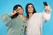 Cheerful twin girls making selfie isolated on blue background. Family. Spending time.
