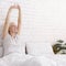 Cheerful well-slept senior lady stretching in bed in morning