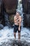 A cheerful wet man in shorts bathes in a river under a waterfall