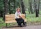 The cheerful woman of average years sits on a bench with autumn maple leaves in hands