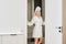 Cheerful woman in bathrobe standing in doorway of bathroom