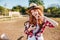 Cheerful woman cowgirl using cell phone and showing peace sign