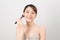 Cheerful woman is doing make up on her face using brush. Beauty routine on white background