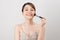 Cheerful woman is doing make up on her face using brush. Beauty routine on white background