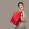 Cheerful woman in evening dress holding red shopping bags.