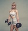 Cheerful woman in fitness wear, exercising with dumbbell. Bodybuilder smiling. Smiling joyful girl with white hair holding big bla