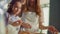 Cheerful woman and girl cracking eggs in mixing bowl on domestic kitchen