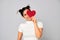 Cheerful woman in love with funny hairstyle holding a small red sparkling heart valentine and covering one eye while