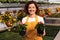 Cheerful woman with potted flowers in greenhouse