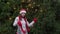 Cheerful woman in Santa hat with red scarf and mittens is happy and dancing on a background of Christmas tree in