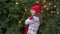 Cheerful woman in santa hat with red scarf and mittens is happy and jumping against the background of Christmas tree in