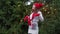 Cheerful woman in santa hat with red scarf and mittens is happy and jumping against the background of Christmas tree in