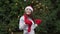 Cheerful woman in santa hat with red scarf and mittens is happy and jumping against the background of Christmas tree in