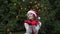 Cheerful woman in Santa hat with red scarf and mittens is happy and jumping against the background of Christmas tree in