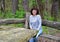 The cheerful woman sits in the wood at a wooden table. The tourist parking for a picnic