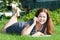Cheerful woman speaking with cellphone while lying on green meadow in summer garden, book is on the grass